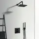 Schwarzer Duschkopf und Thermostat von Ideal Standard an einer hellen Wand, daneben eine Halterung für Handtücher und eine Handbrause.